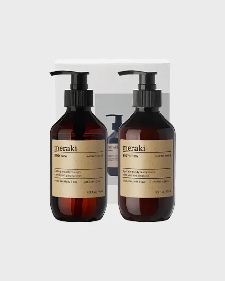 Dos botellas Meraki de color ámbar oscuro con dosificadores negros, una de gel de baño y otra de loción corporal, sobre un fondo gris claro.
