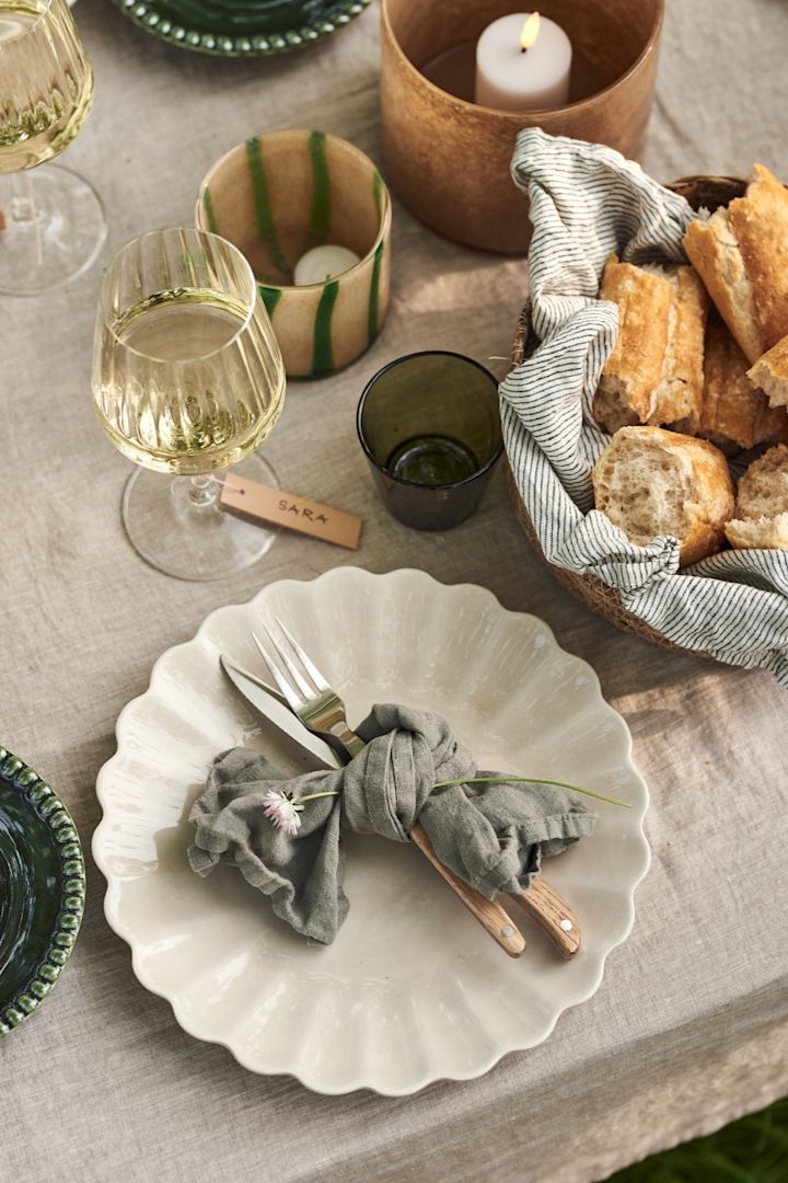 Pon la mesa en pleno verano: aquí con un plato Oyster beige de Mateus, cubiertos envueltos en una servilleta de tela y copas de vino blanco sobre una mesa puesta.
