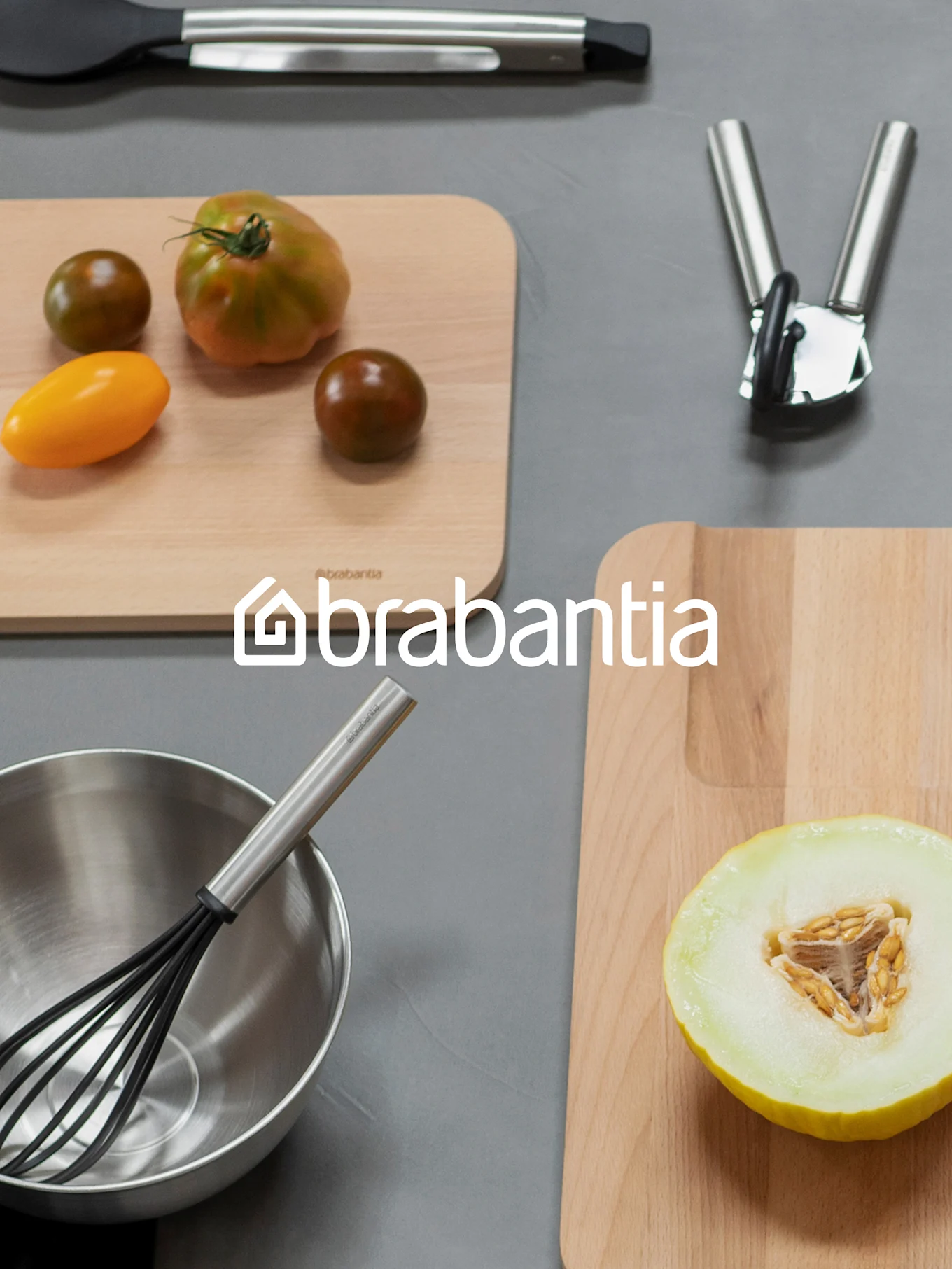 Logotipo de Brabantia sobre una vista aérea de artículos de cocina, incluyendo tablas de cortar con tomates y melón, un batidor en un tazón y otros utensilios.