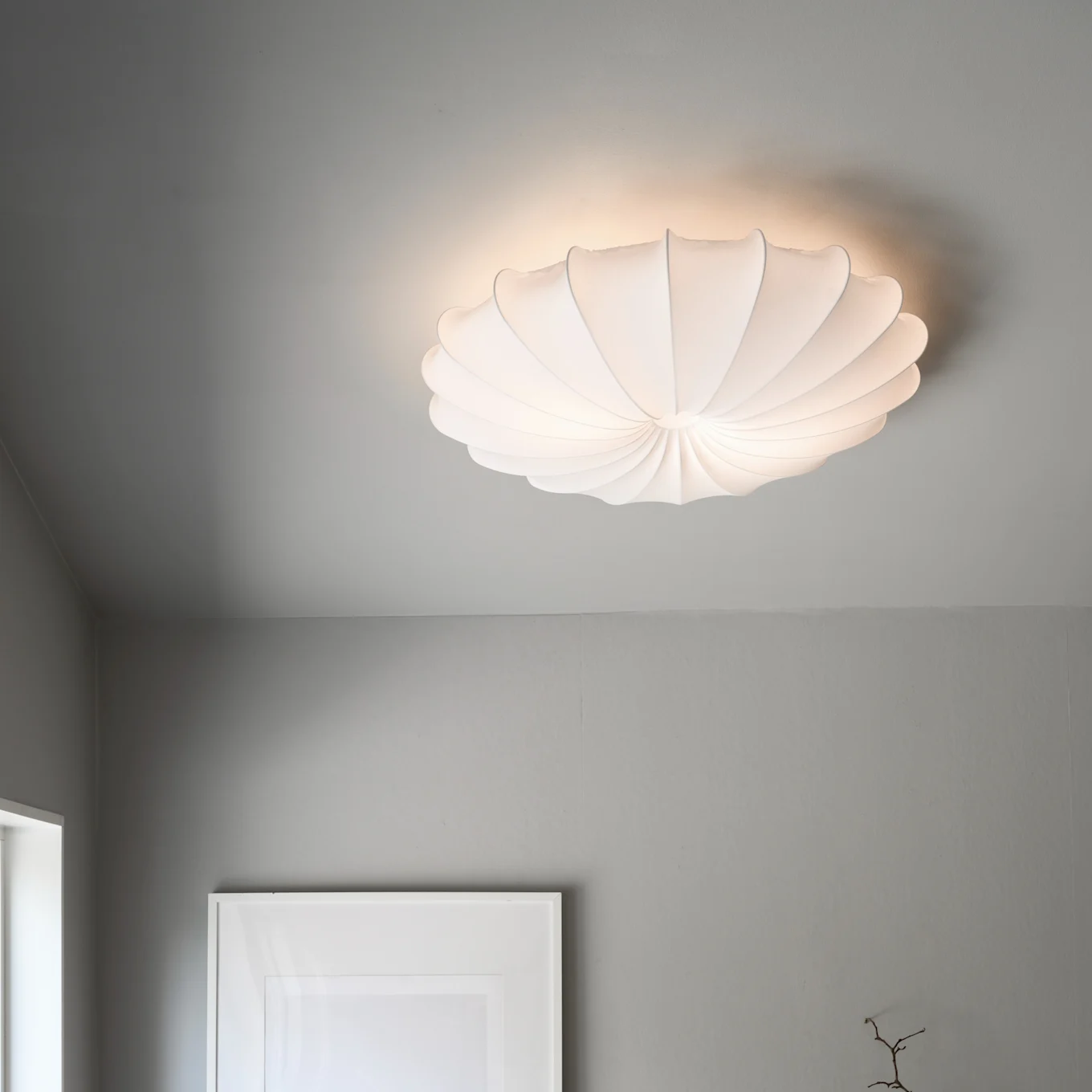 Una lámpara de techo blanca, plisada y en forma de concha ilumina un techo gris.