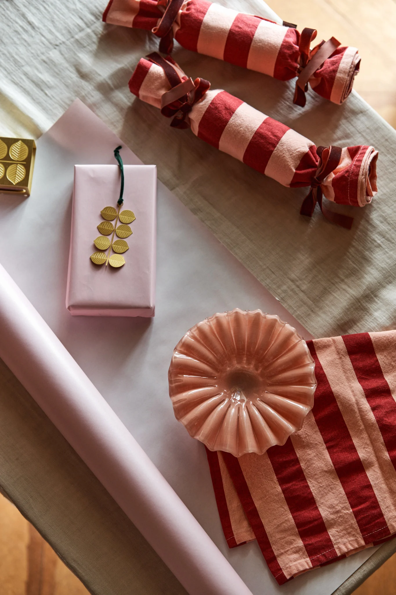 Aquí esperan un cuenco rosa de Byon y un adorno dorado de Pluto, listos para ser envueltos en paños de cocina a rayas y papel rosa: una forma creativa de celebrar el primer domingo de Adviento.