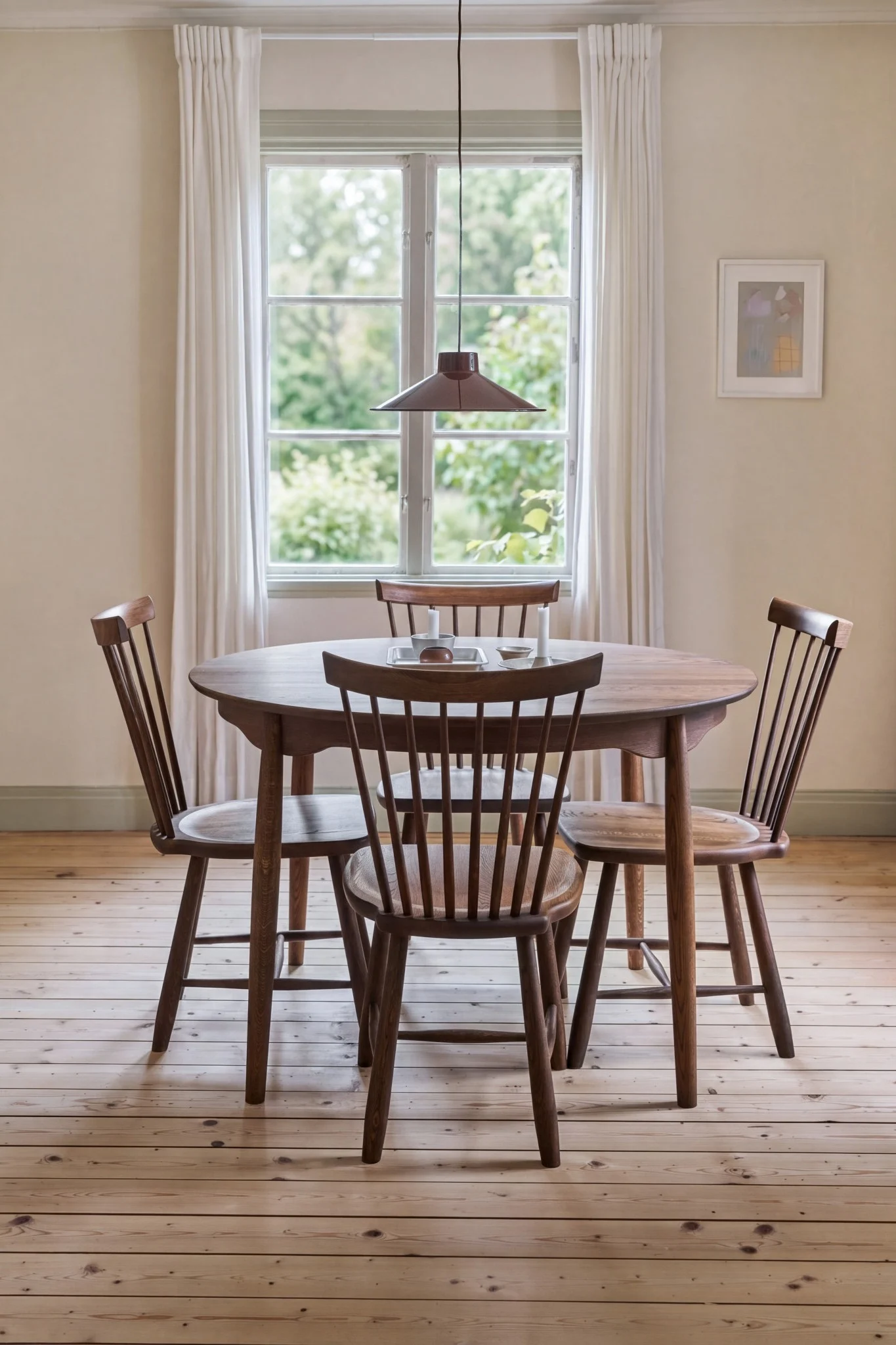 Un acogedor comedor con una mesa redonda de madera, cuatro sillas de madera, una ventana con cortinas blancas y una lámpara colgante.