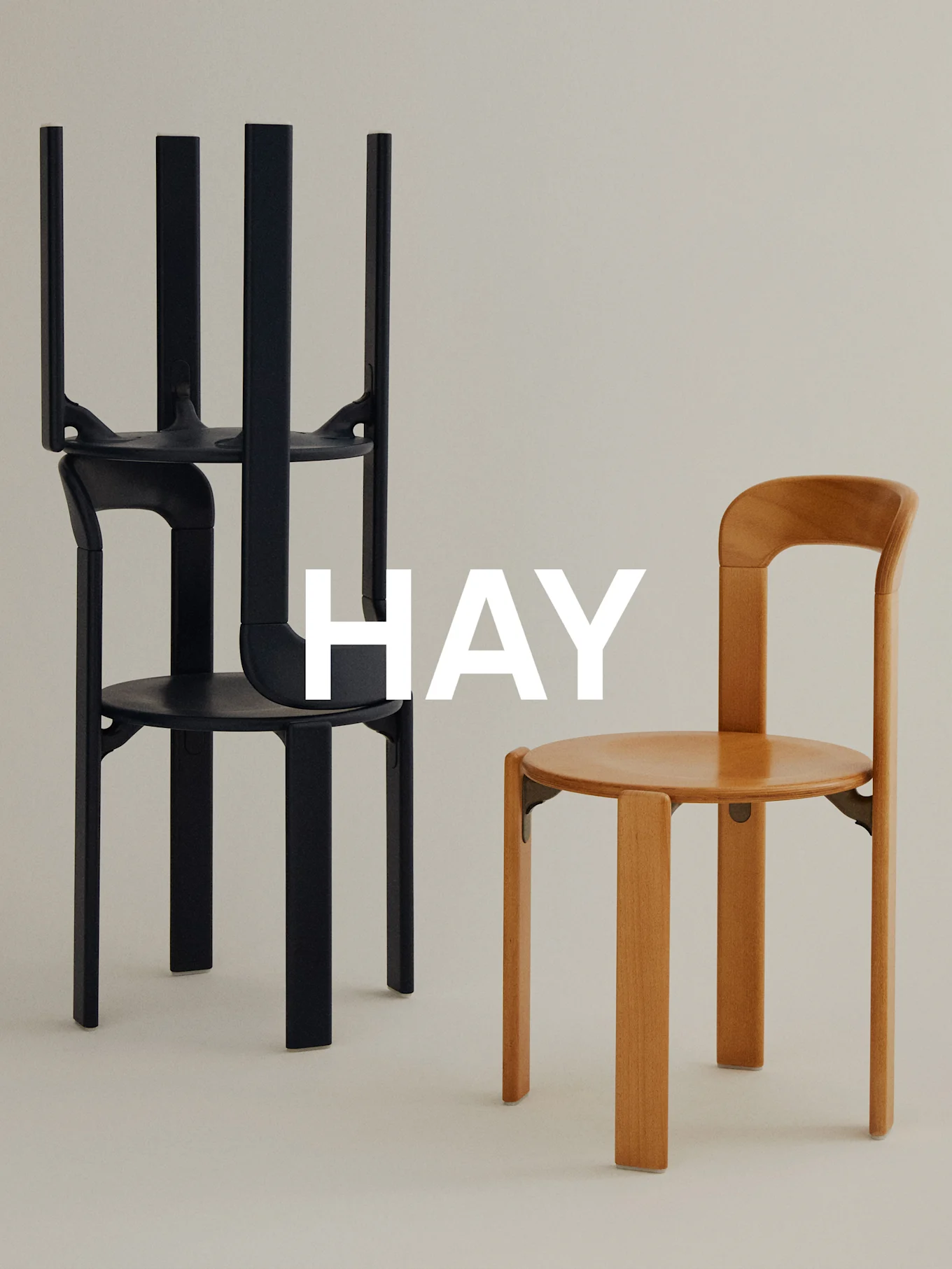 Dos sillas minimalistas sobre fondo claro, una negra apilada, una marrón clara de pie, con superposición 'HAY'.