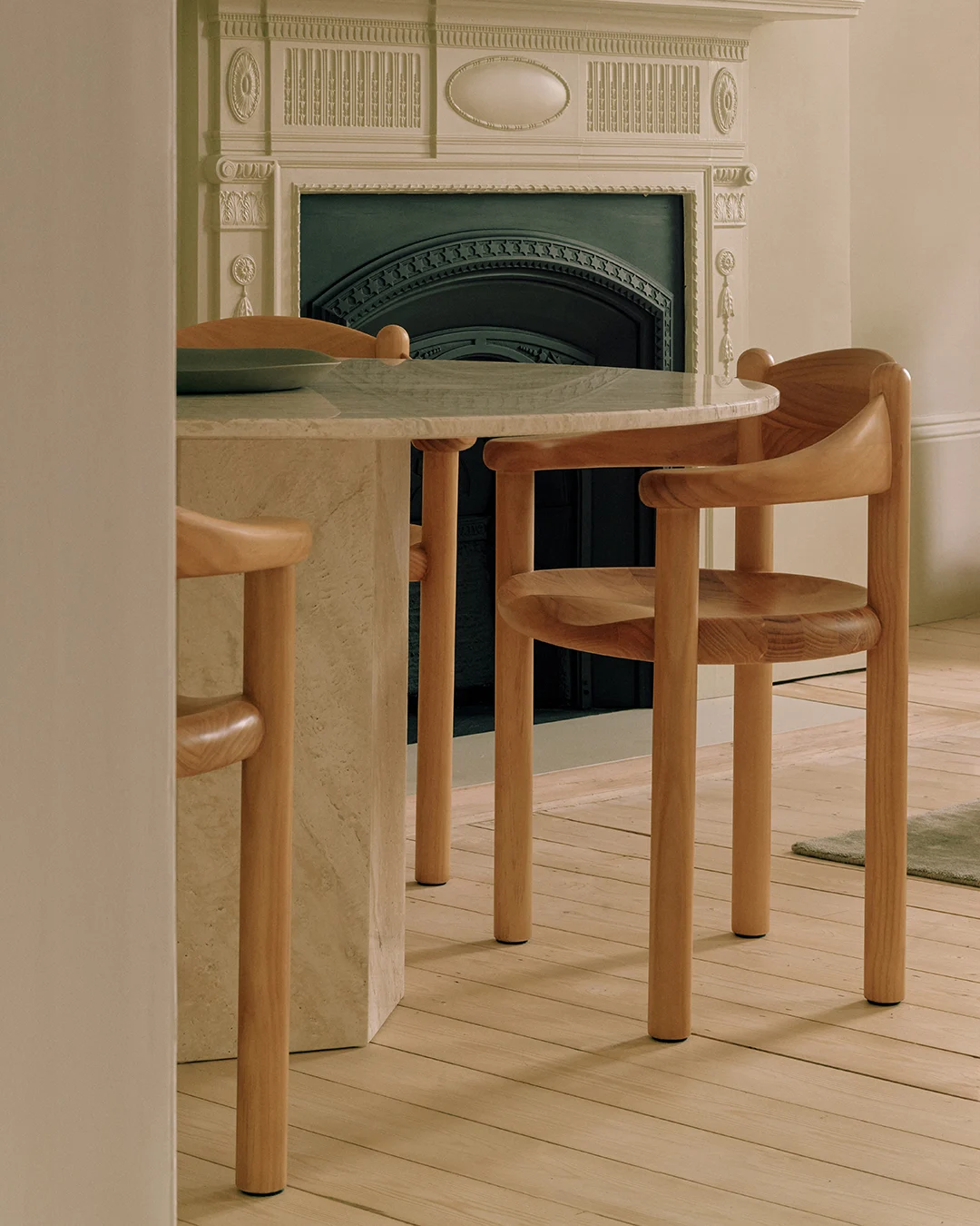 Una mesa redonda de mármol con dos sillas de madera clara, frente a una chimenea decorativa.