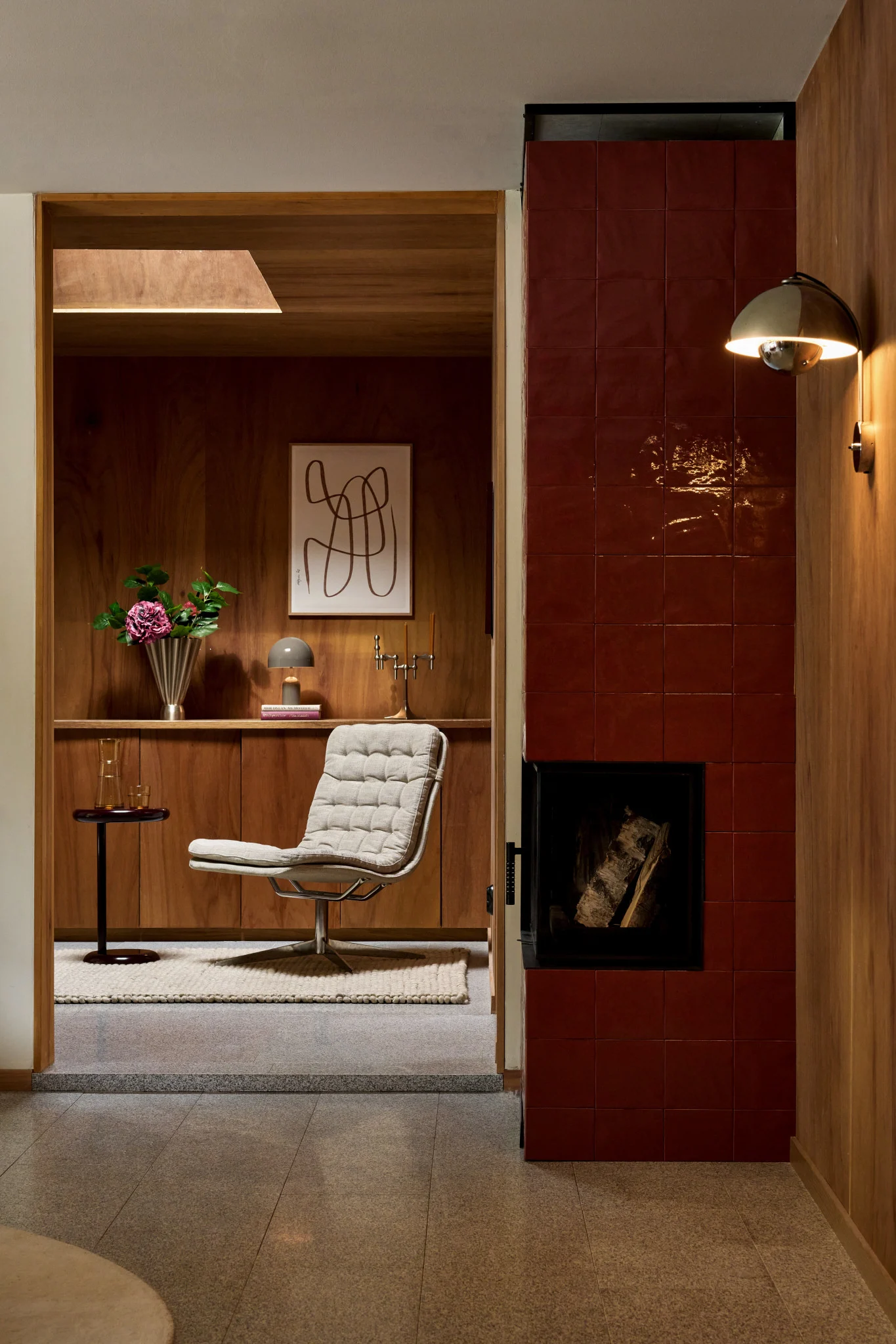 Un interior acogedor con un sillón texturizado, paredes de madera, una chimenea de azulejos rojos y un aplique de pared dorado.