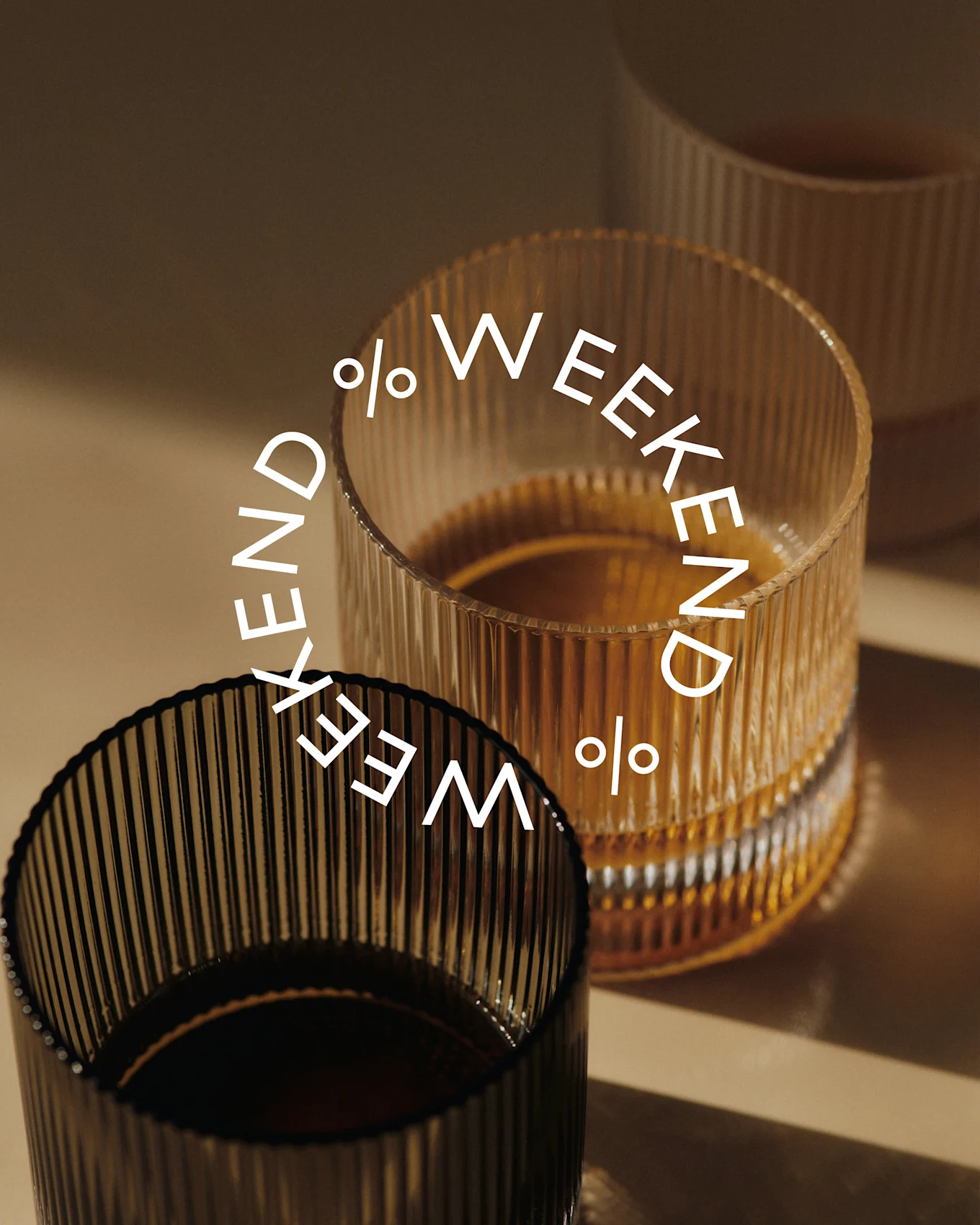 Tres vasos acanalados, dos llenos de líquido oscuro. Un vaso oscuro en primer plano, uno ámbar detrás. Texto: Weekend %.