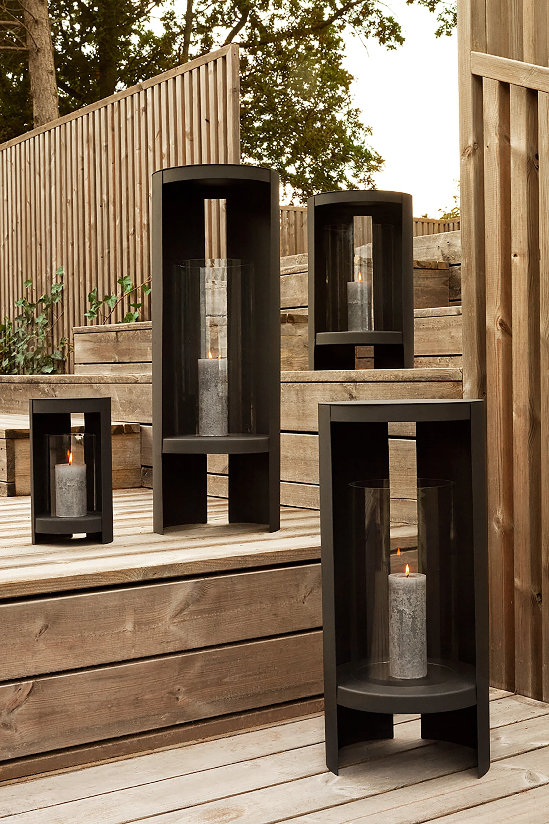 Faroles y portavelas para exteriores: aquí puedes ver el farol Oro de AYTM en negro y en varios tamaños sobre una escalera de madera en un jardín.