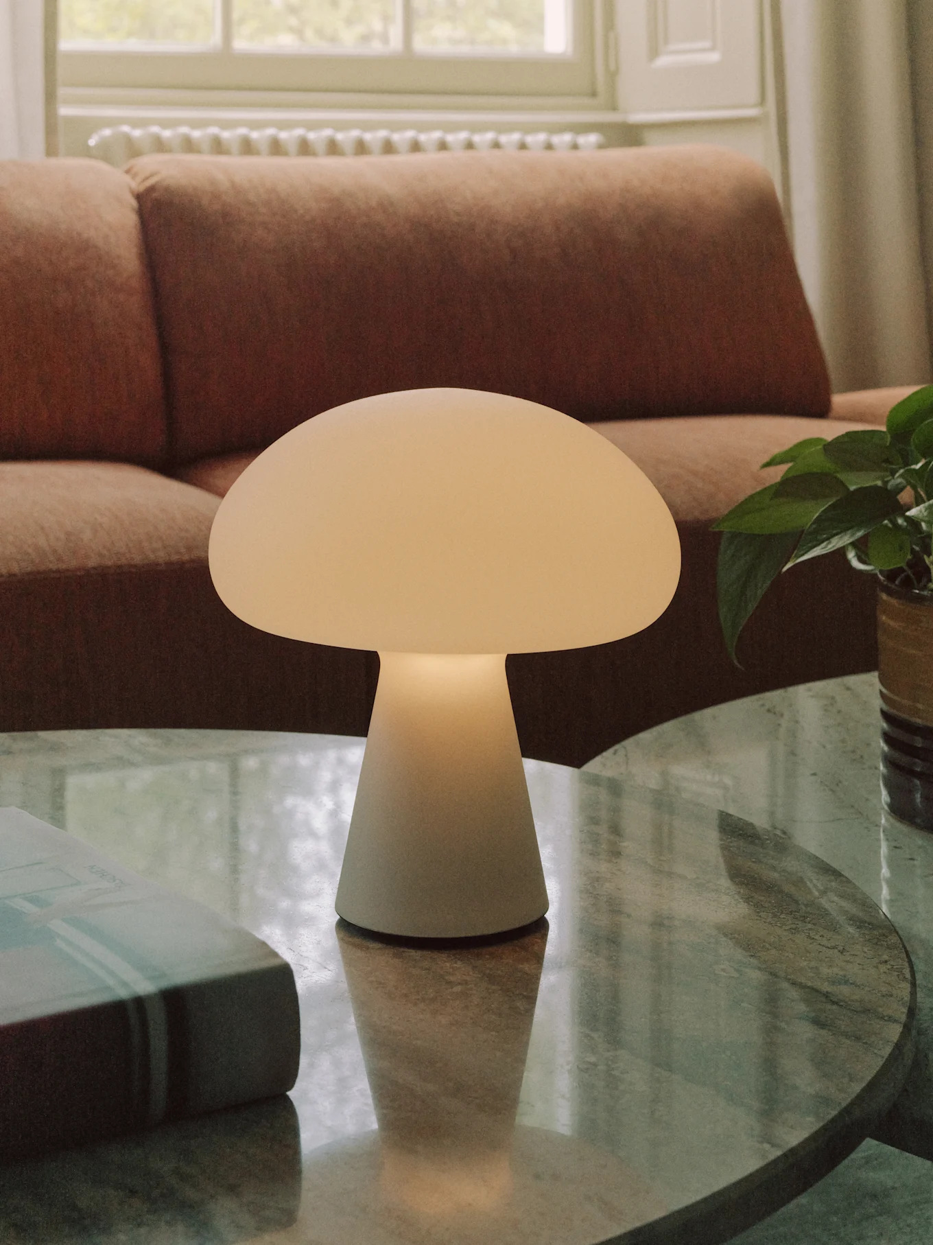 Una lámpara de mesa en forma de seta de color blanco roto sobre una mesa de centro redonda de mármol en una sala de estar.