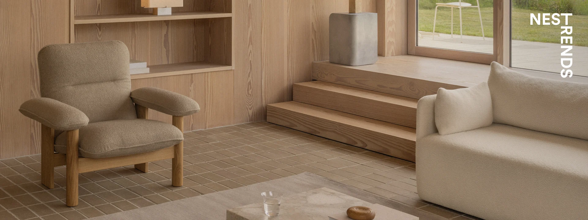 Una sala de estar moderna con un sillón marrón texturizado, un sofá beige, paneles de madera en la pared, suelo de baldosas y vistas a un jardín.