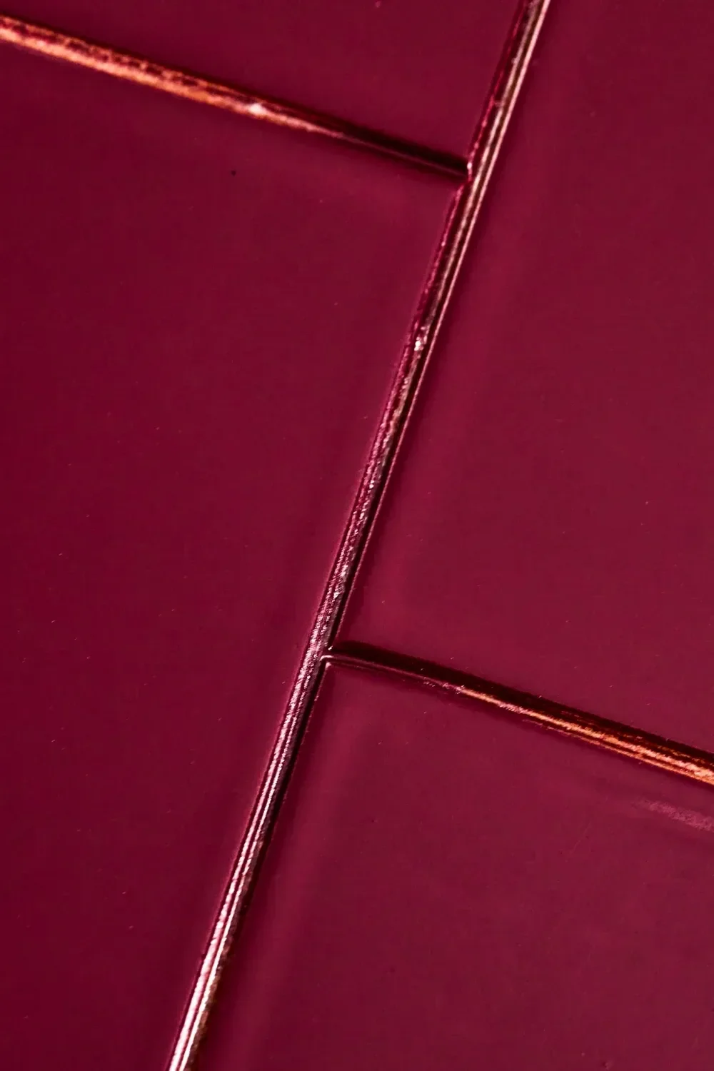 Azulejos rojos oscuros brillantes con juntas metálicas de color marrón rojizo.