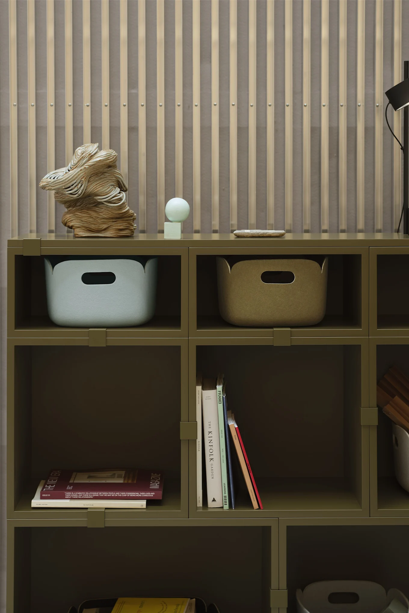 Una estantería verde con cajas de almacenamiento y libros como detalles, completamente en línea con las tendencias de decoración de 2026.