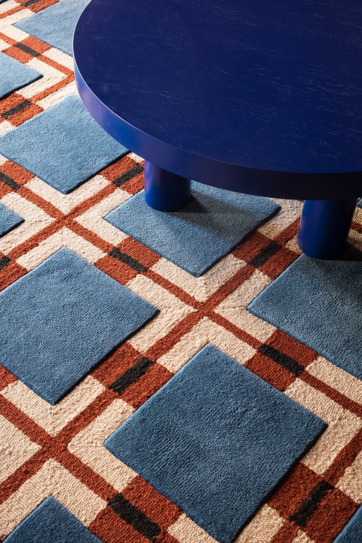 La combinación de color y patrón en textiles y alfombras es una parte importante de las tendencias de diseño de interiores escandinavo en 2024, aquí podemos ver una alfombra de lana roja/azul con un patrón geométrico de Layered.