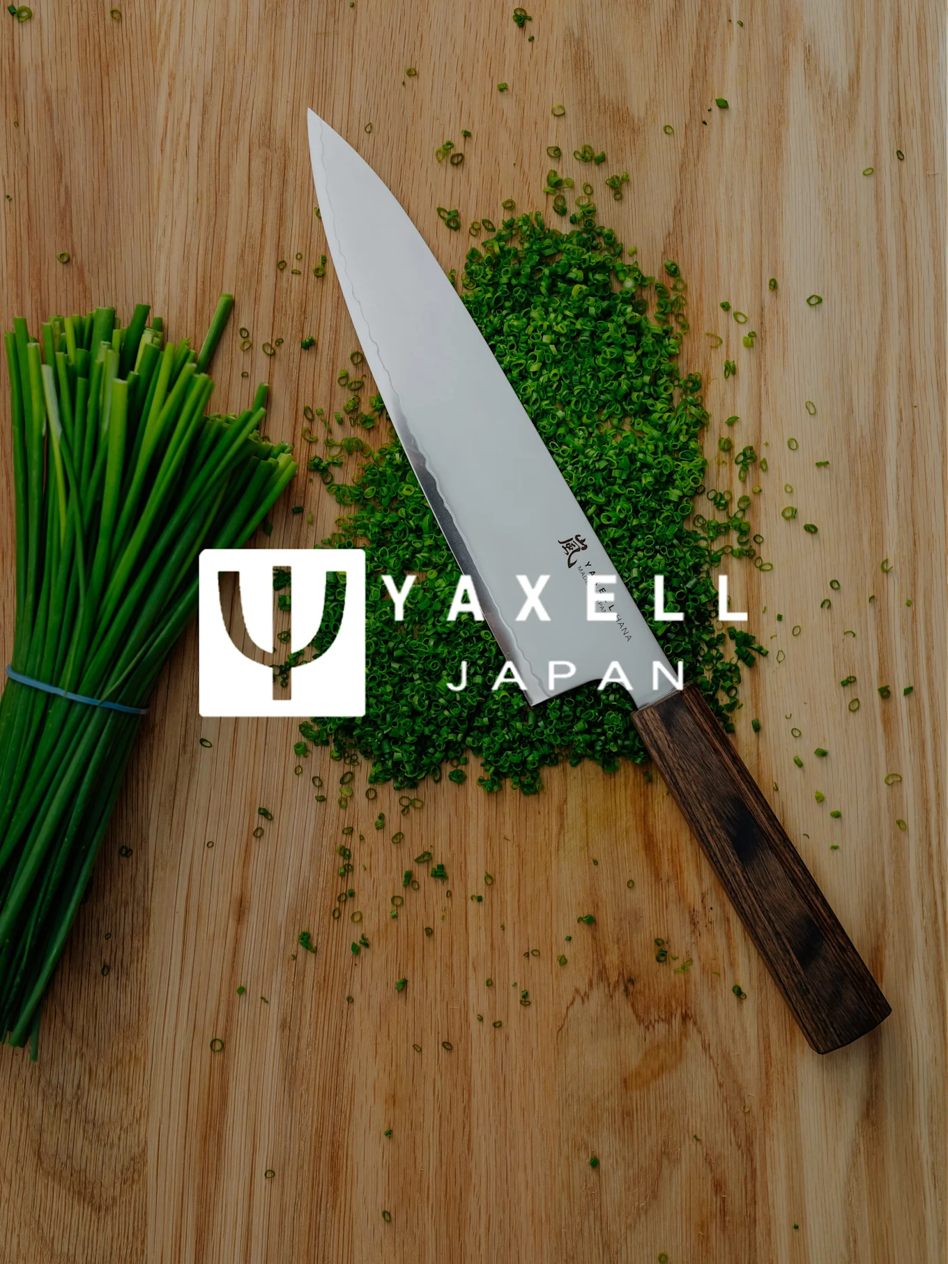 Cuchillo de chef Yaxell, cebollino picado y manojo de cebollino en tabla de madera con logo Yaxell Japan.
