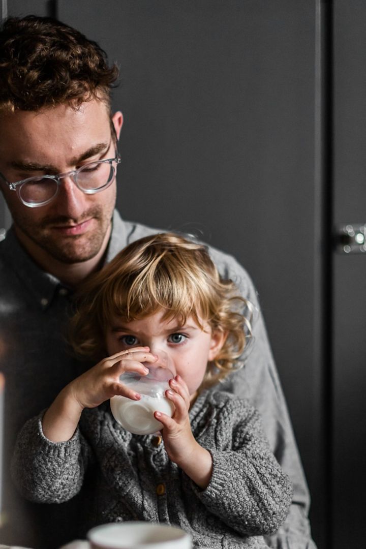 El tiempo juntos es sin duda el regalo más valioso para el Día del Padre. En esta imagen, vemos a un niño pequeño sentado en el regazo de su padre, bebiendo de un vaso de Scandi Living.
