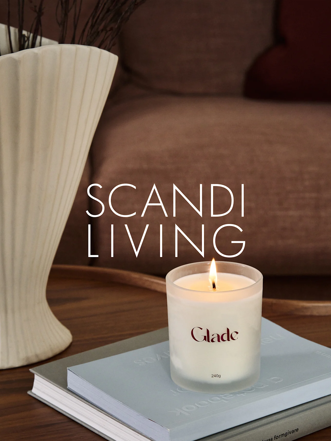 Una vela Glade encendida sobre libros, junto a un jarrón estriado con ramas. Texto superpuesto: SCANDI LIVING.