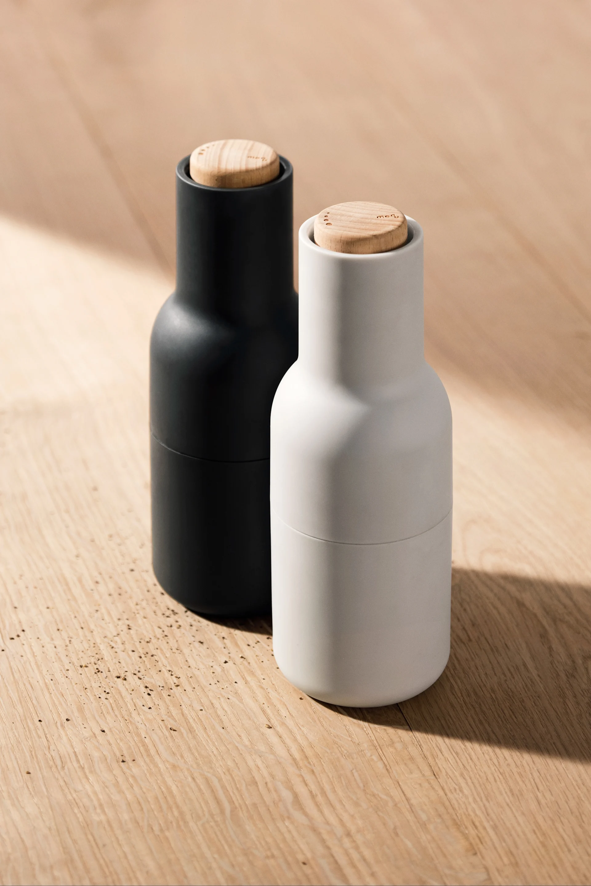 Aquí se pueden ver dos de los Bottle Grinder de Audo Copenhagen sobre una mesa de madera.