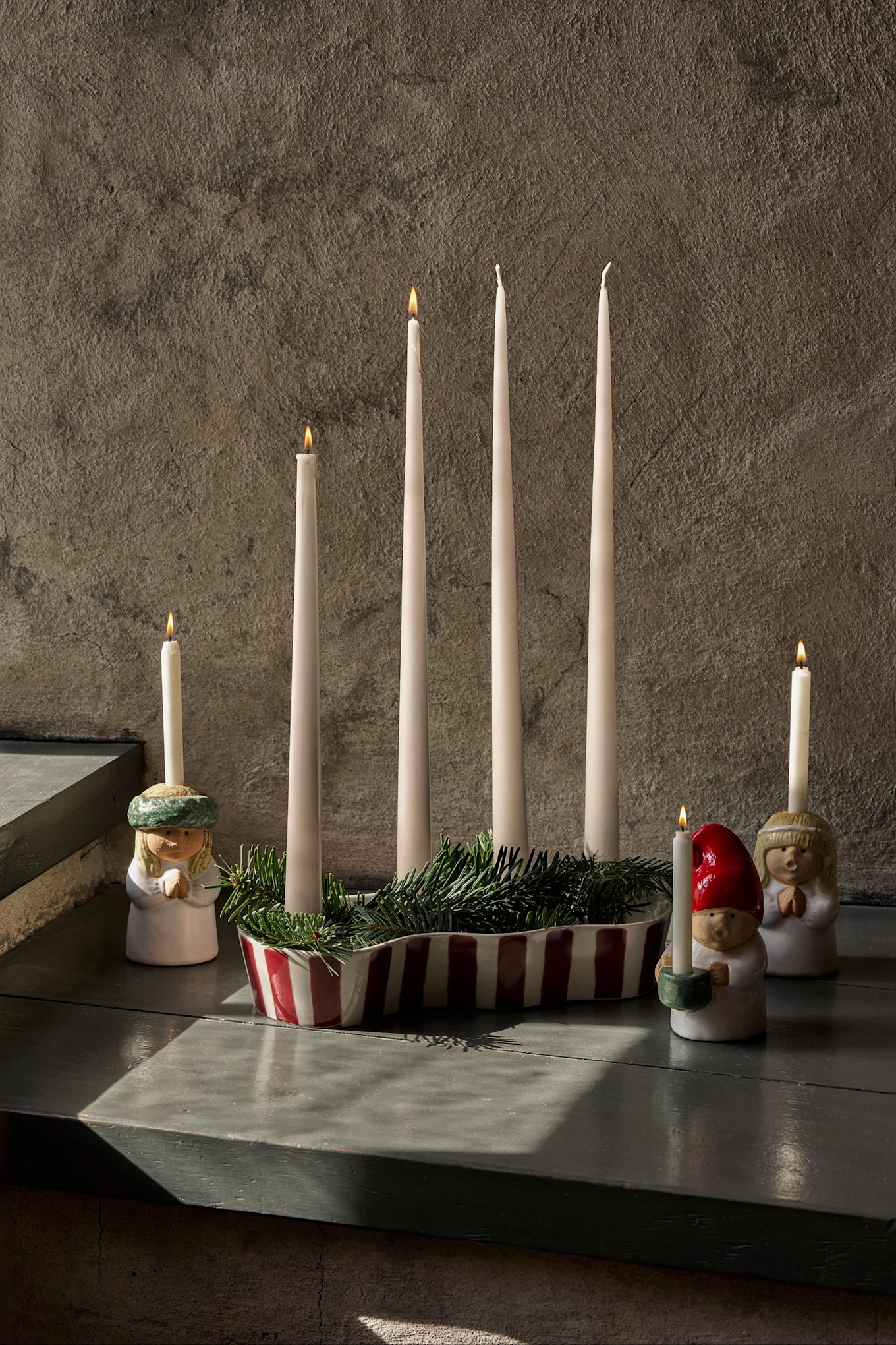 Decoración de Adviento con cuatro velas sin encender, abeto verde y tres figuras con velas encendidas.