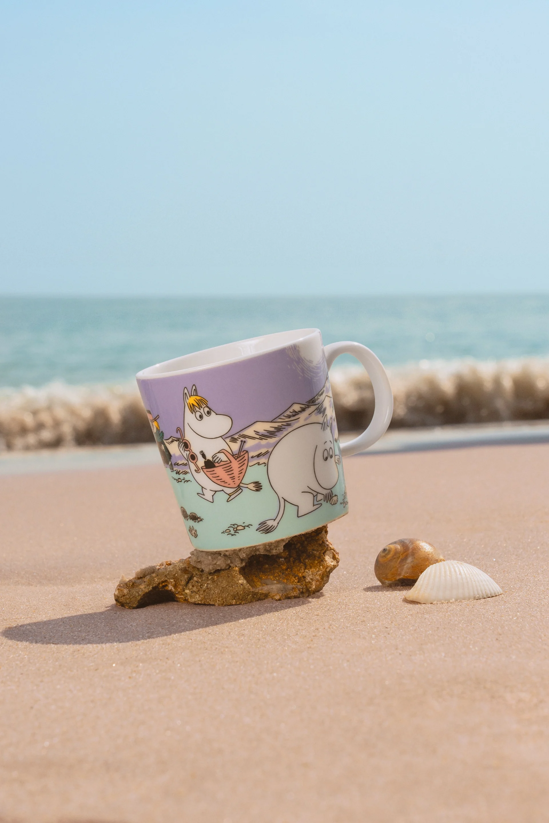 La taza Mumin del verano 2025, "Beach Day" está de pie en una playa de arena.