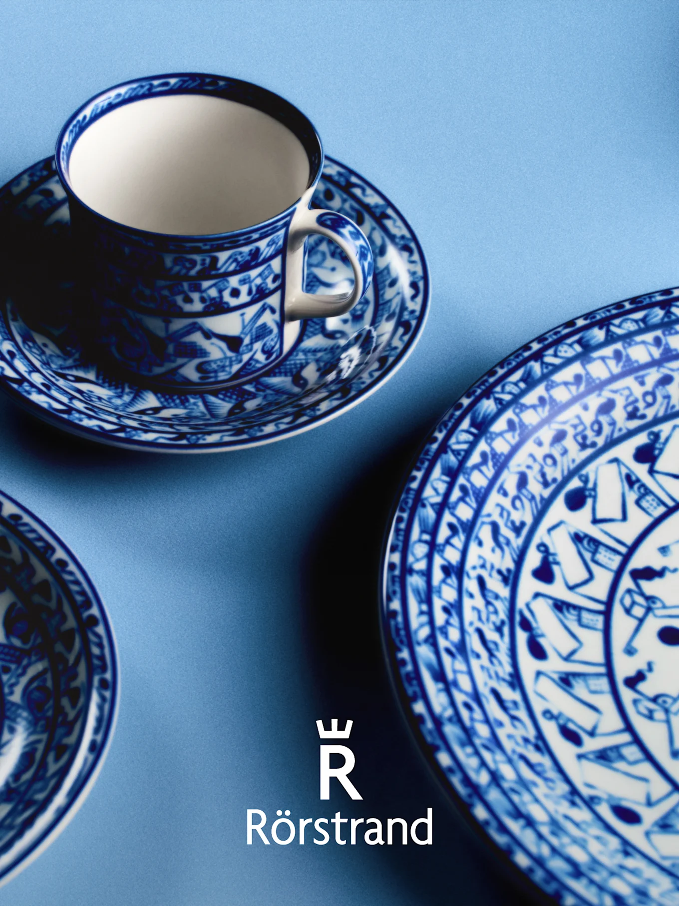 Taza de té, platillo y plato con diseño azul y blanco sobre fondo azul claro, con logo de Rörstrand.