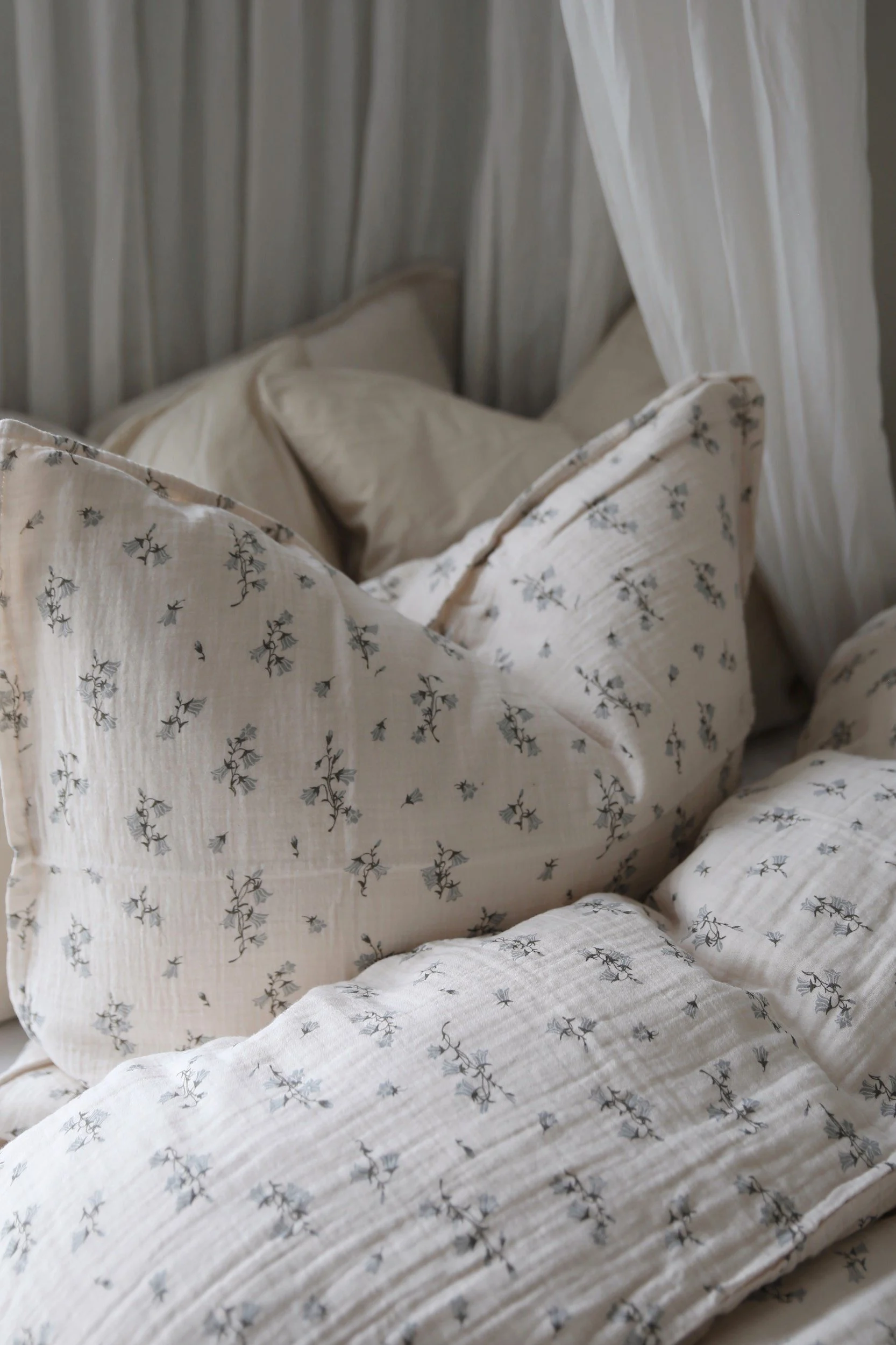 Ropa de cama acogedora con una tela beige claro y un delicado estampado floral azul y cortinas blancas.