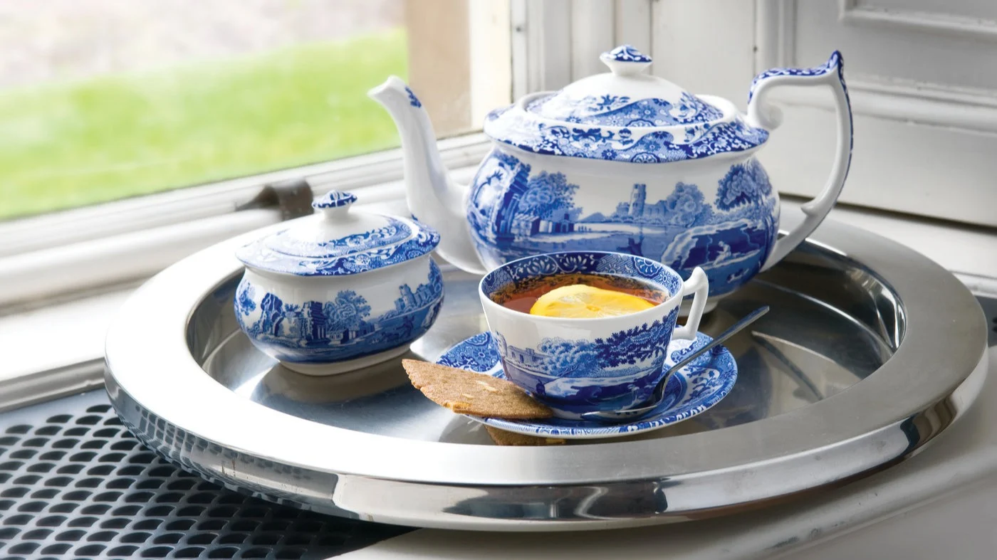 Juego de té de porcelana azul y blanca con paisaje en una bandeja de plata. Incluye tetera, azucarero y taza de té con té, limón y una galleta.