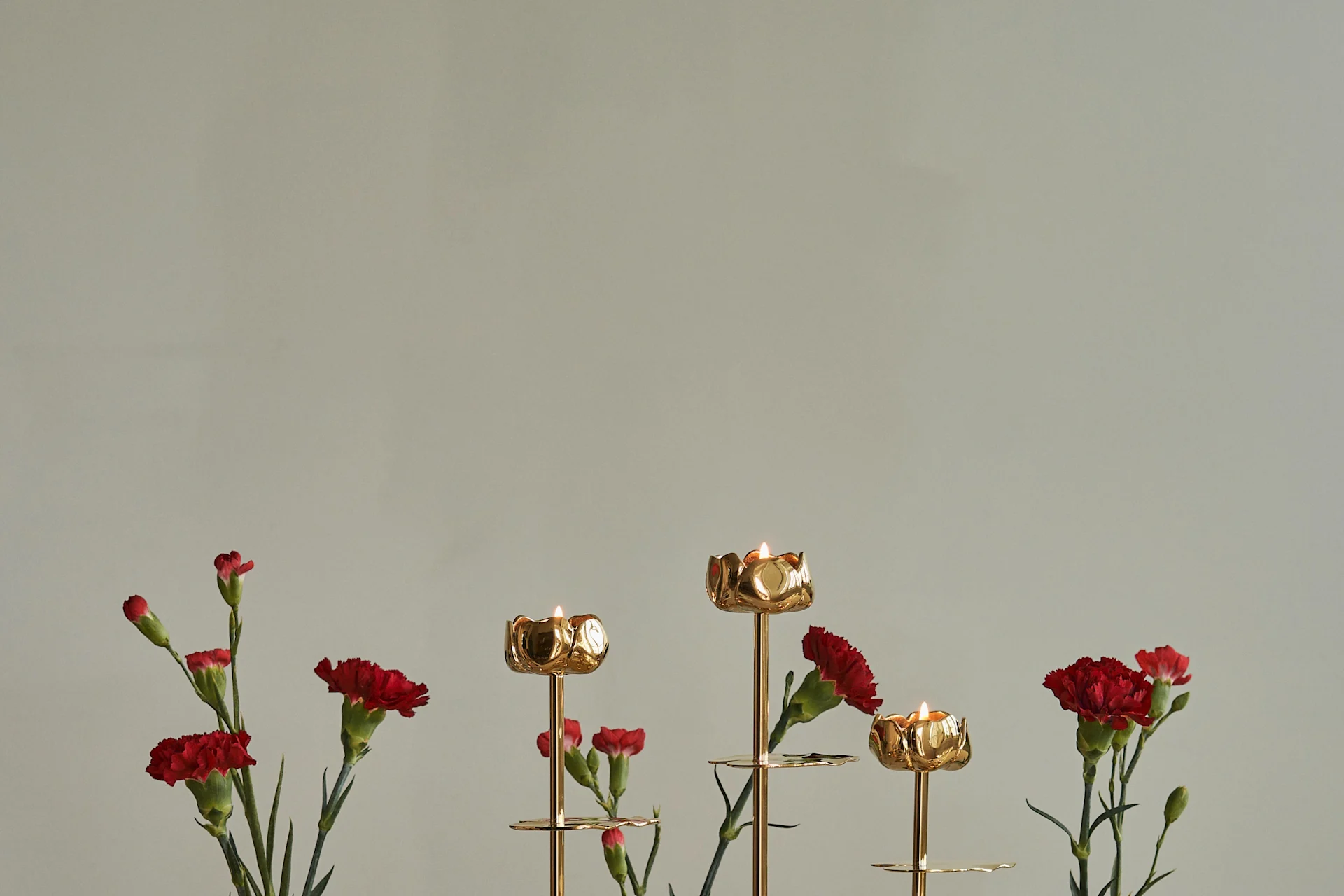 Candelabros dorados en forma de flor con velas encendidas y claveles rojos.