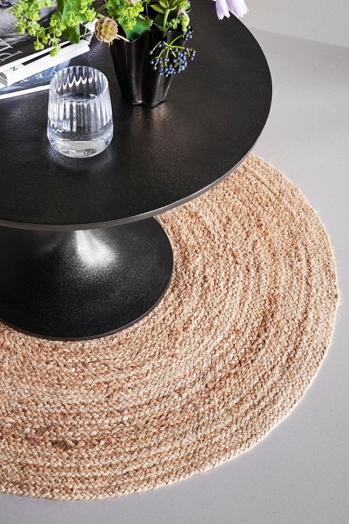 La alfombra redonda de yute Rugy de House Doctor, ideal para una decoración boho gracias a su material, se encuentra bajo una mesa redonda negra.