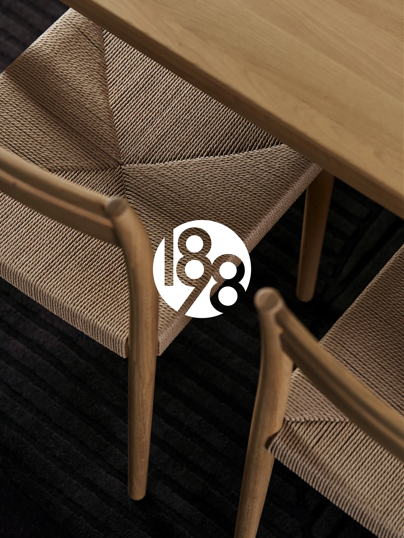 Dos sillas de madera con asientos trenzados, una mesa de madera y una alfombra oscura. Logotipo blanco '188' superpuesto.