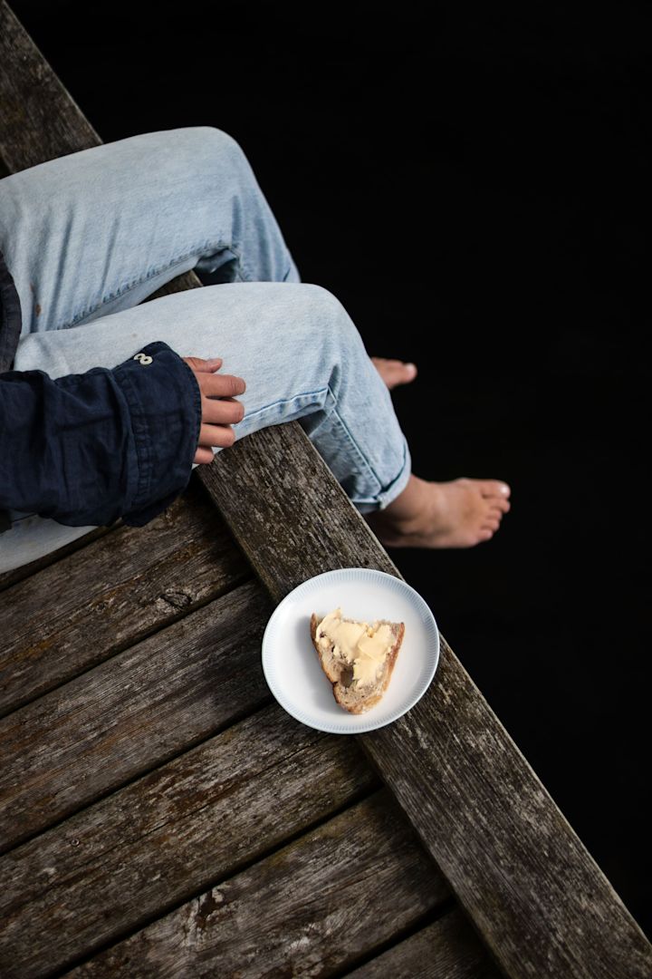 Lagom: una mujer sentada en un embarcadero, junto a un plato de Osean de Wik&Walsoe con un bocadillo.