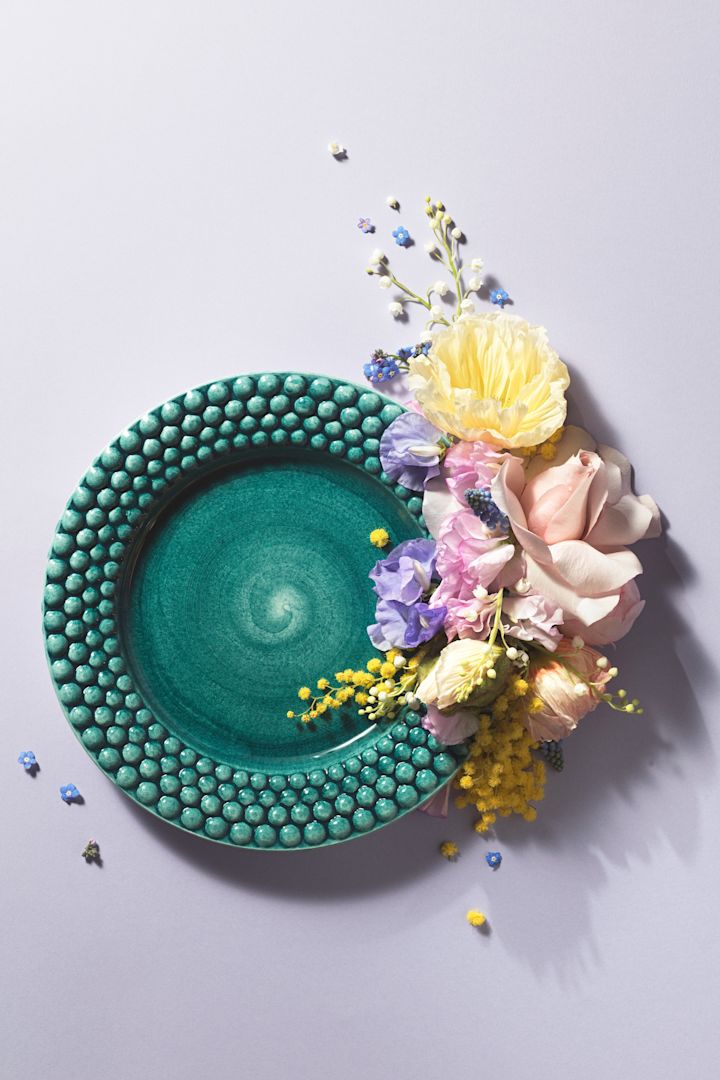 Un plato de la colección Bubbles en color Ocean de Mateus, ingeniosamente colocado con flores para una foto.
