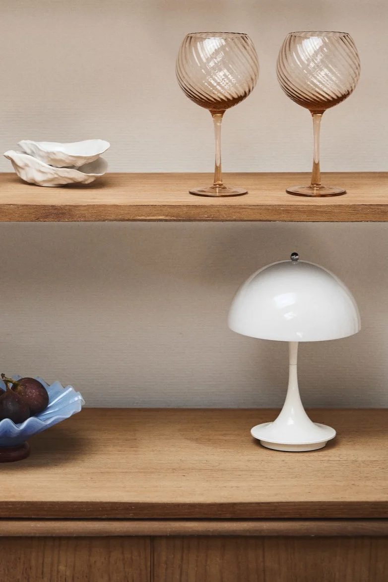 Renueva tu hogar con ideas de iluminación moderna como la Panthella mini de Louis Poulsen, vista aquí en un vitrina de madera con copas de vino rosado y un tazón azul.