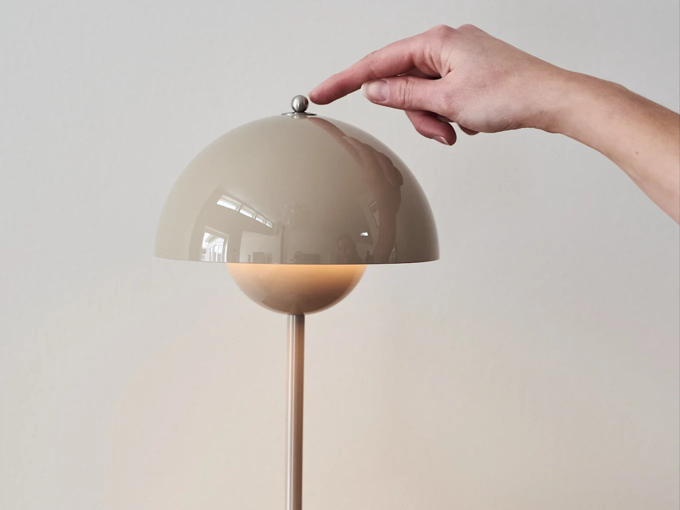 Mano presionando un botón metálico en una lámpara beige con forma de cúpula, que emite un brillo cálido.