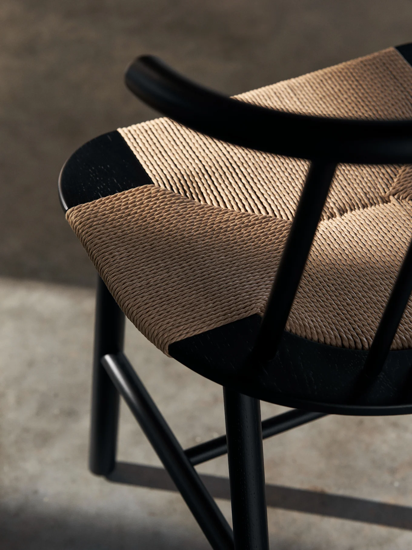 Primer plano de una silla de madera negra con un asiento tejido en color tostado claro y patrón diagonal. Las sombras caen sobre el asiento texturizado.