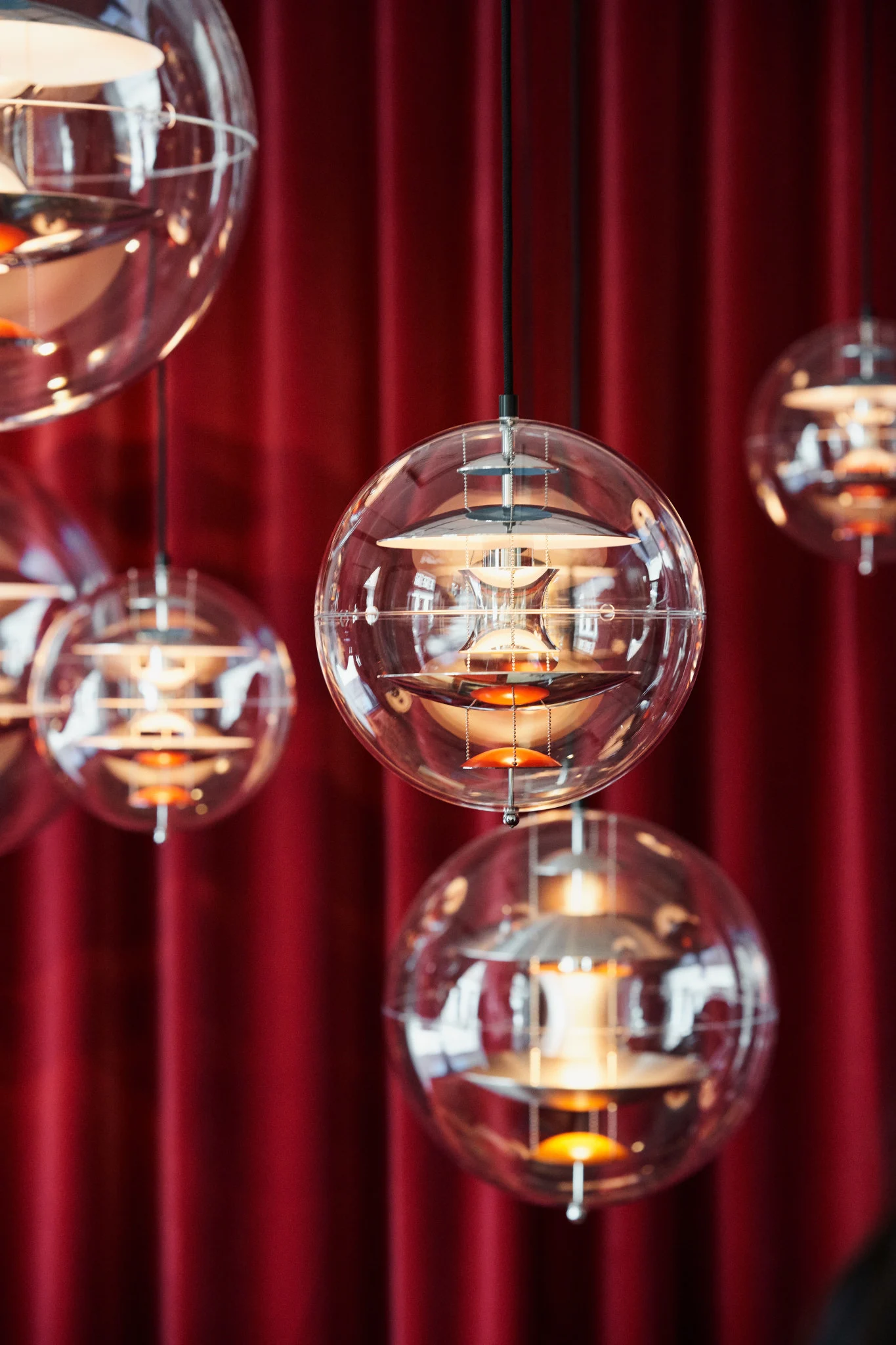 Varias lámparas colgantes Globe Glass de Verpan cuelgan del techo frente a una cortina roja.