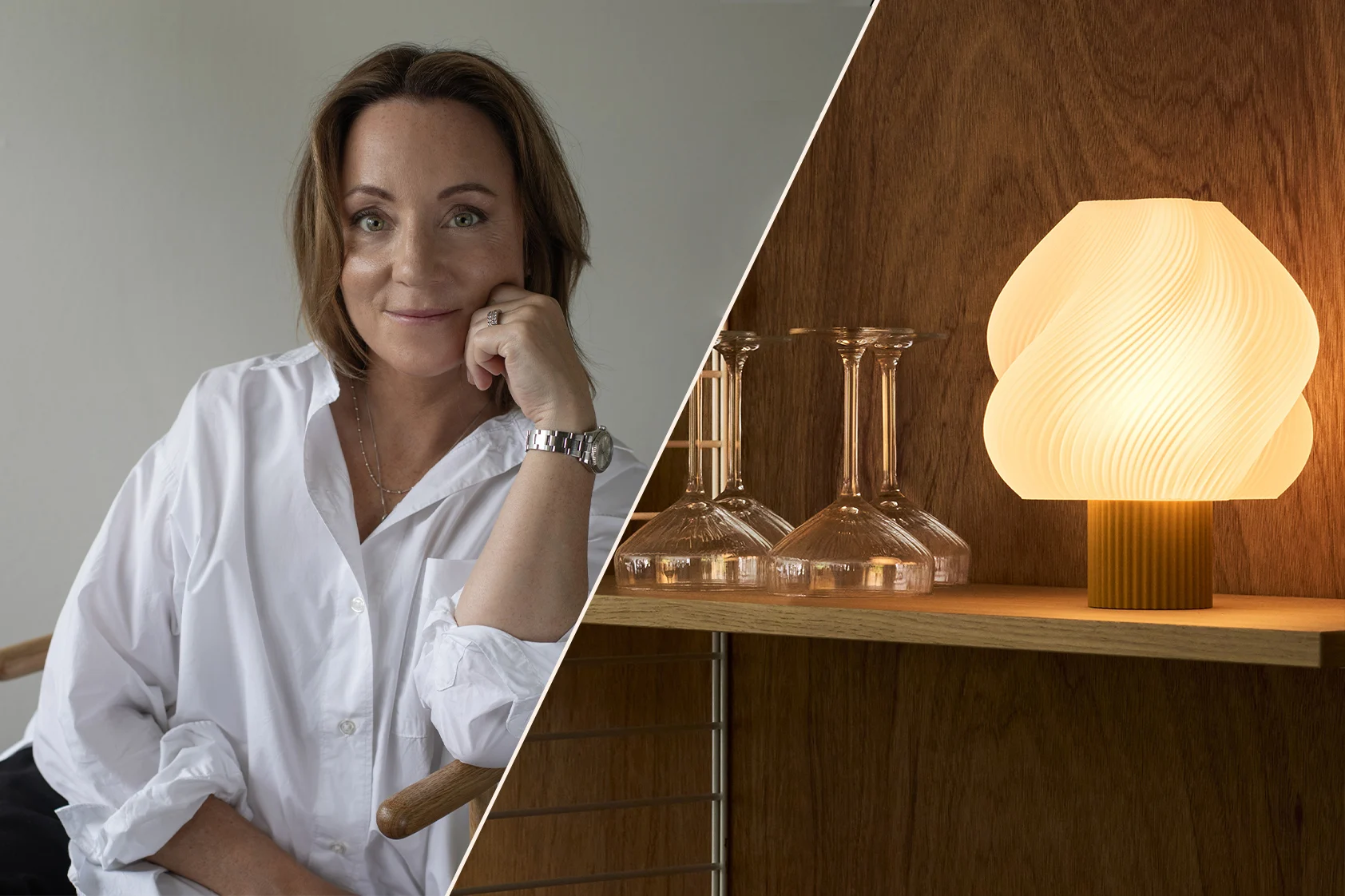 Mujer sonriente con camisa blanca, barbilla apoyada en la mano, con un reloj, en un interior cálido y moderno con estantes y una lámpara.
