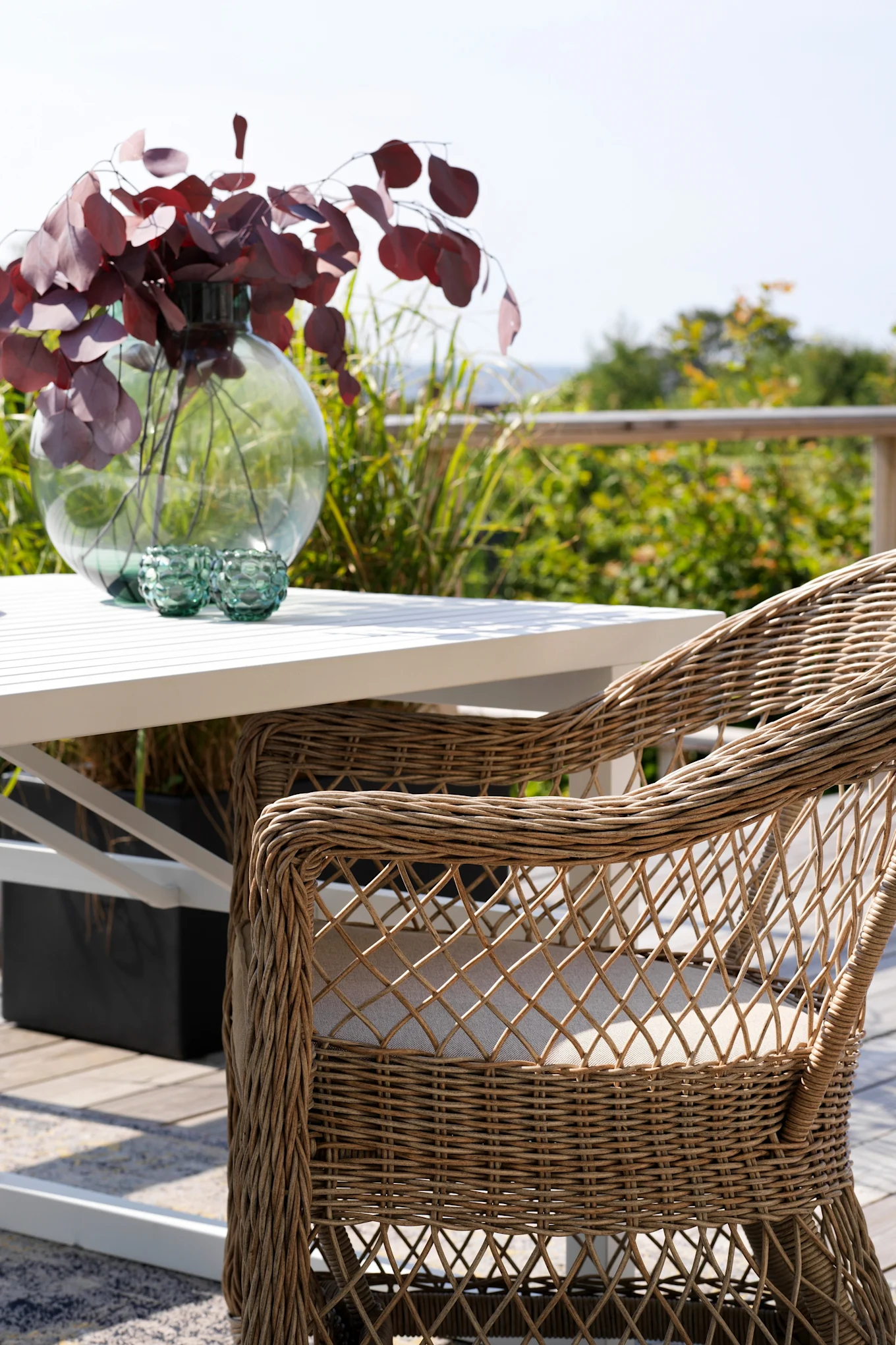 La silla con reposabrazos Kamomill de Brafab se encuentra en una terraza junto a una mesa.
