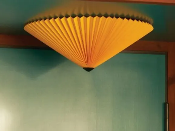 Accesorio de techo cónico plisado amarillo sobre una pared verde azulado.