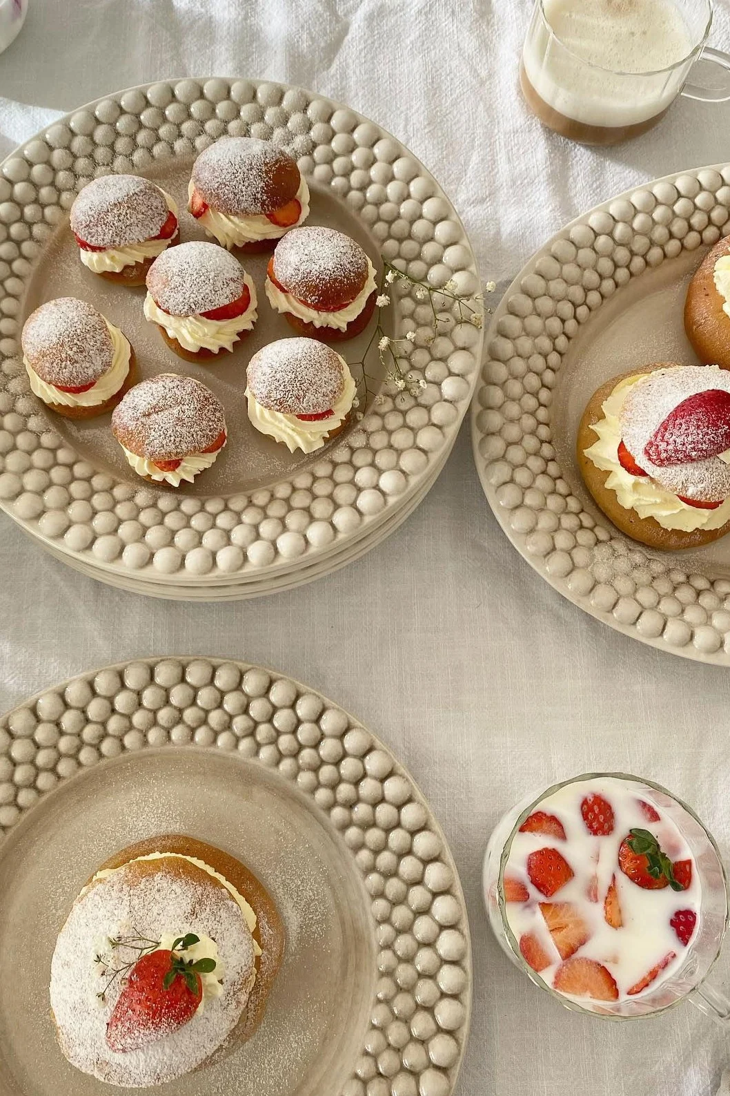 Bollos de crema con nata montada, fresas y azúcar glas en platos texturizados, con bebidas.