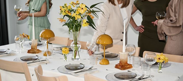 Cómo organizar una fiesta con una auténtica atmósfera festiva. Aquí ves una mesa decorada con toques amarillos y invitados socializando alrededor de la mesa.