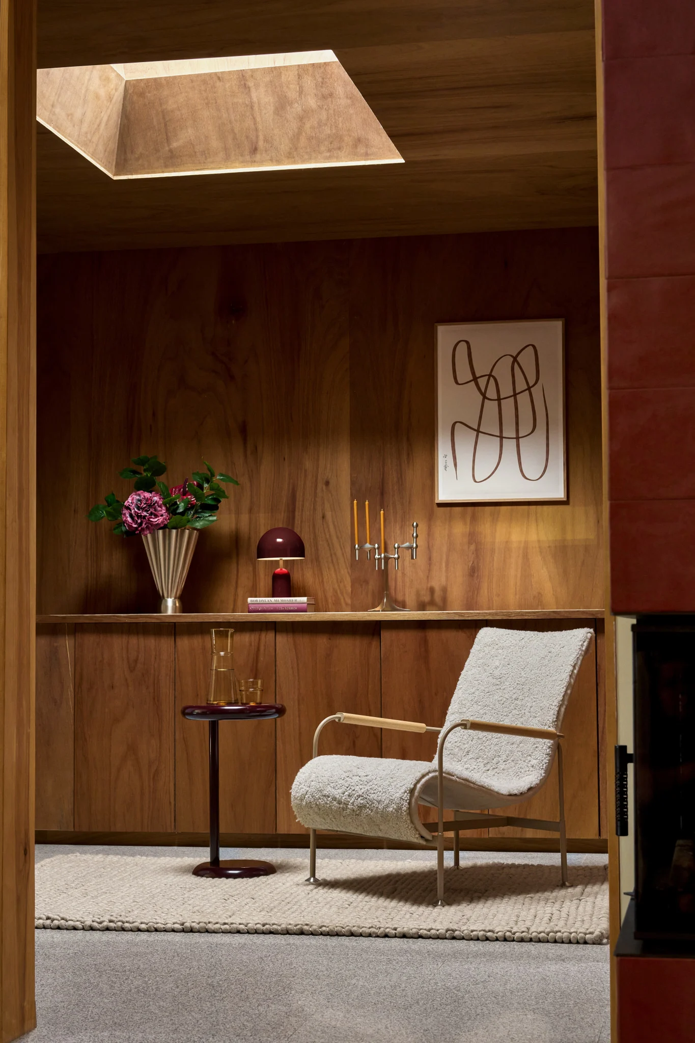 Acogedora habitación con paredes de madera, sillón bouclé crema, mesa auxiliar, flores y arte abstracto.