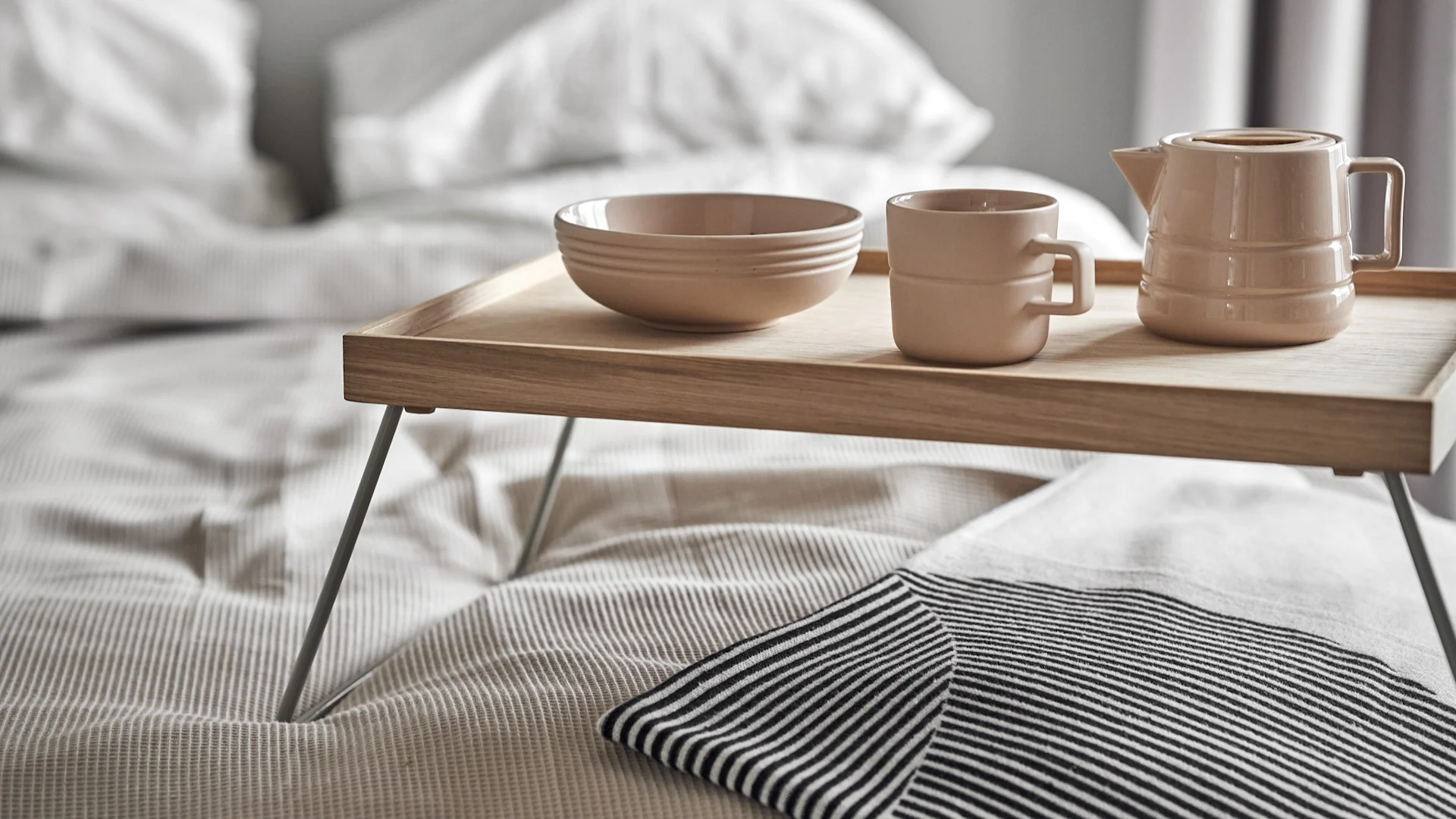 Lagom también significa empezar el día de forma relajada. Aquí, una taza, una jarra y un bol de la colección Lines de NJRD reposan sobre una bandeja de desayuno en la cama.