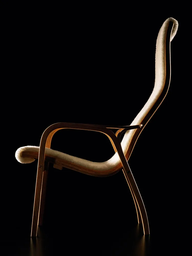 Una elegante butaca con estructura curva de madera clara y tapicería de piel crema, sobre fondo negro.