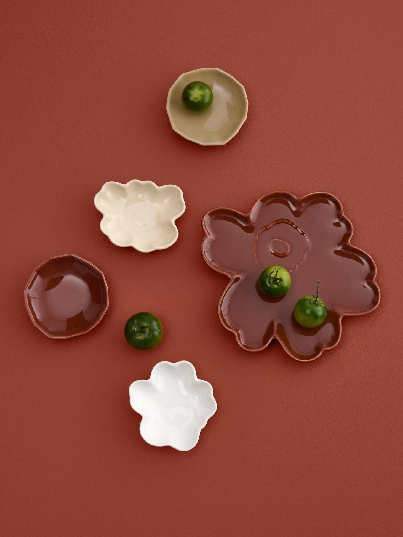 Surtido de platos pequeños de formas irregulares en crema, blanco y marrón con frutas verdes pequeñas, sobre un fondo marrón rojizo.