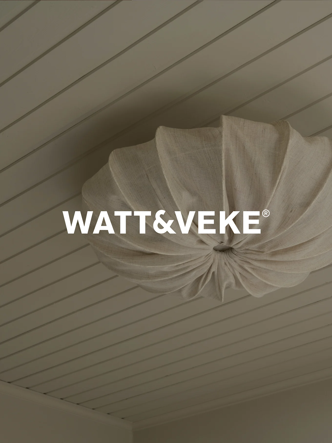 Logo WATT&VEKE® sobre una lámpara de techo plisada de tela natural en un techo de madera clara.