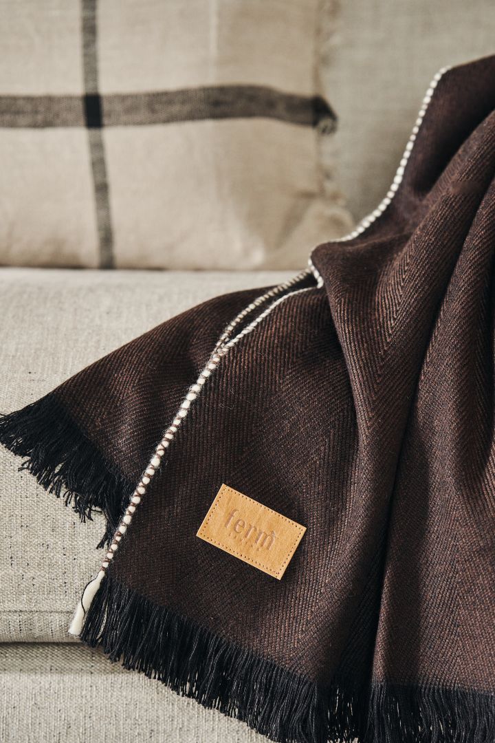 Manta Herringbone  en marrón oscuro de Ferm Living con un primer plano de su preciosa etiqueta.