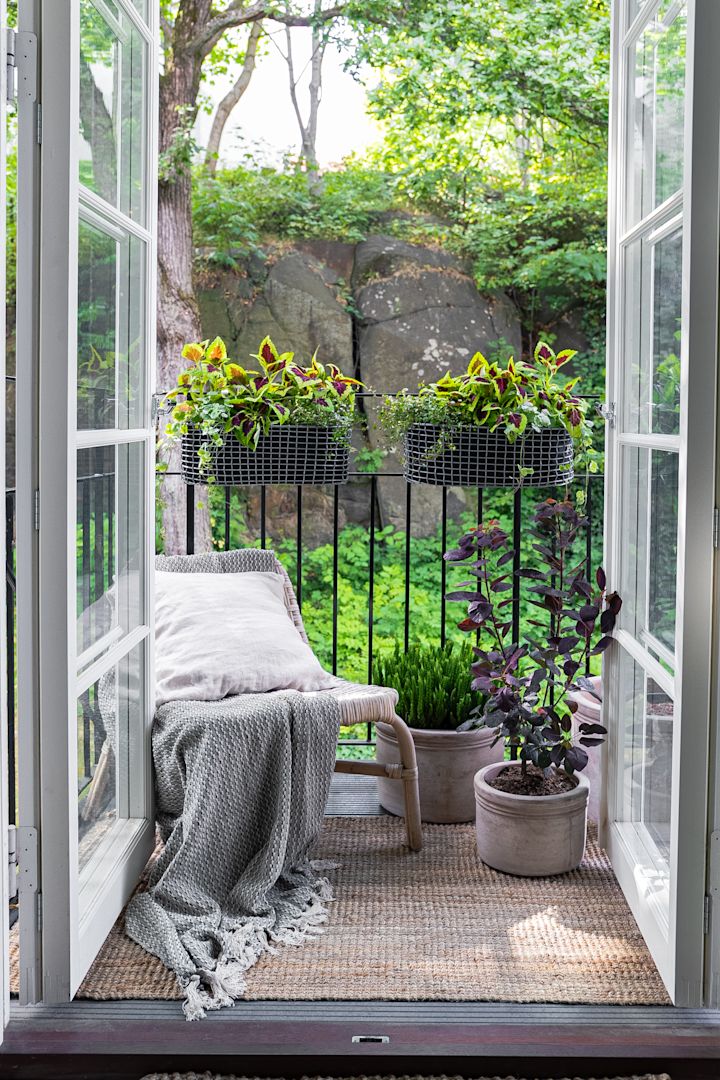 Un pequeño balcón amueblado de forma acogedora con un sillón y varias plantas, incluidas en la cesta de balcón Korbo.