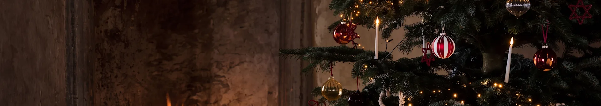 Un árbol de Navidad festivo con adornos y una vela encendida junto a una cálida chimenea con leña ardiendo.