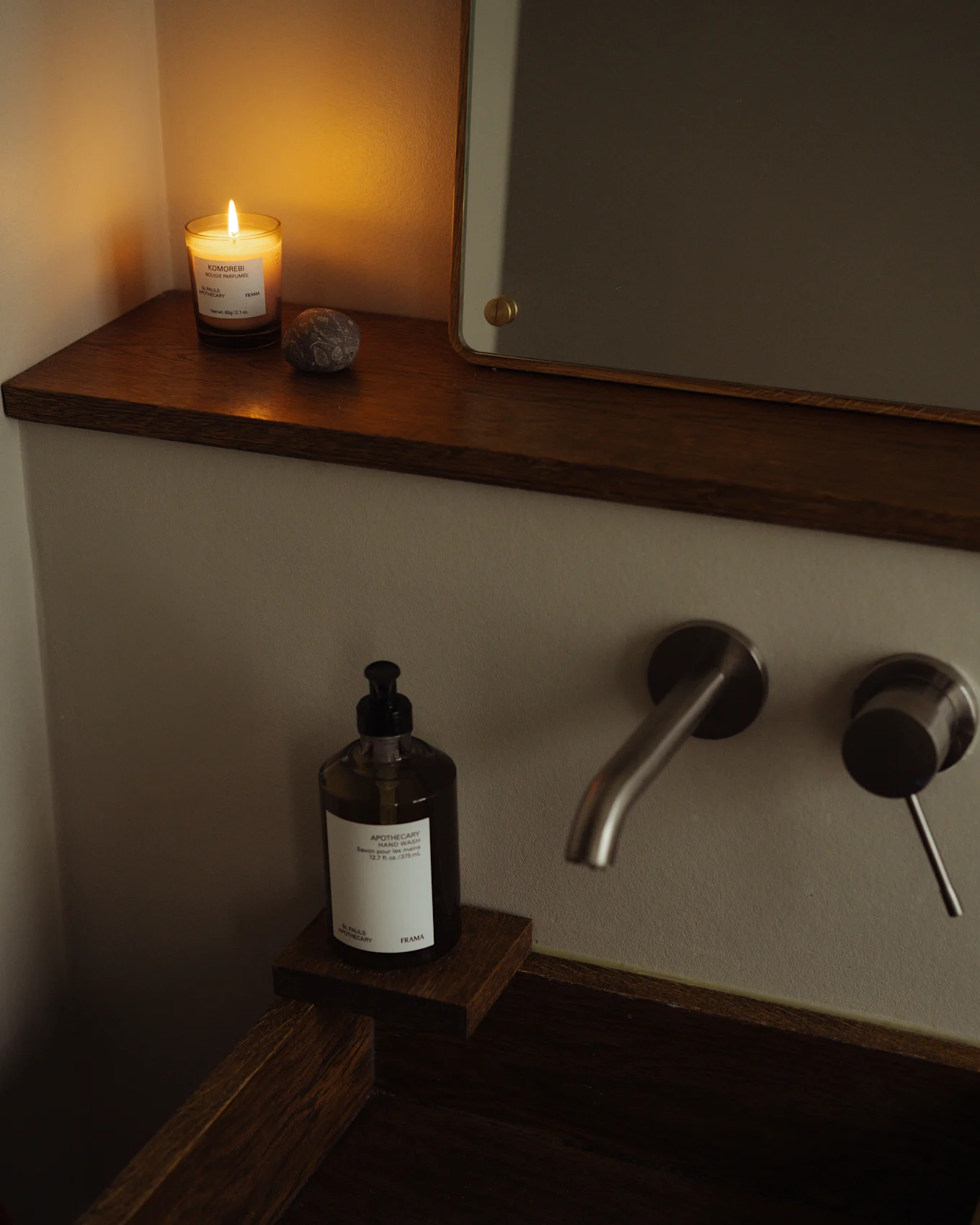 Acogedor baño con vela encendida, botella de jabón de manos y grifo de metal cepillado en un lavabo de madera oscura.