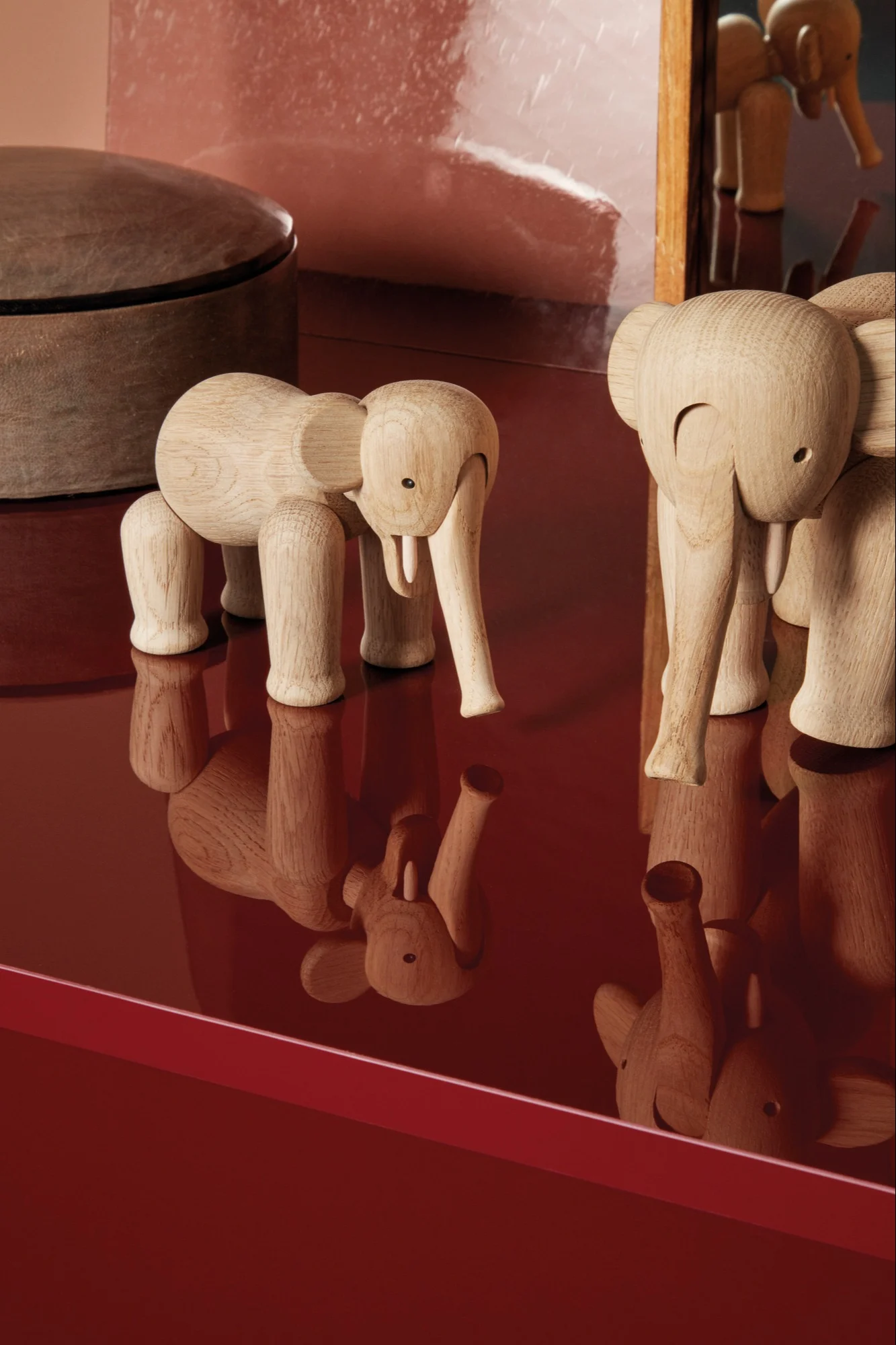Dos figuras de elefante de madera clara de pie sobre una superficie roja reflectante.