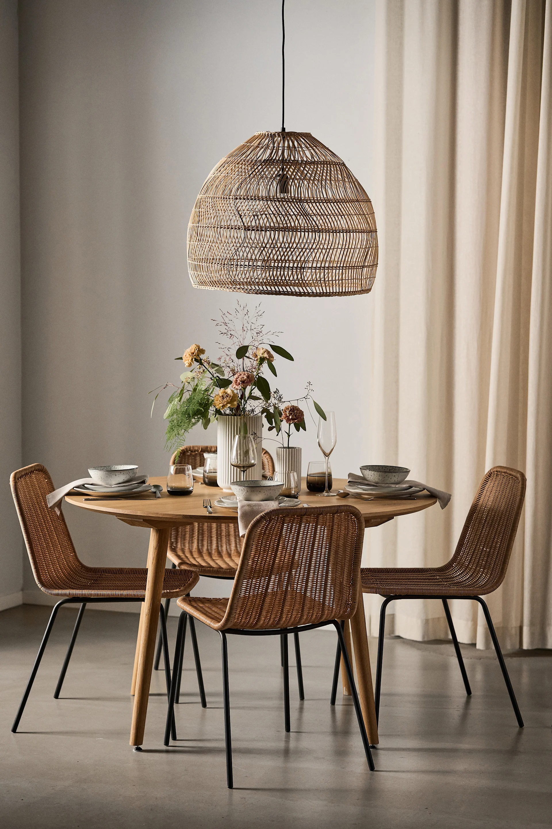 Un comedor de estilo boho con una lámpara de rafia y una mesa redonda con cuatro sillas Hapur de House Doctor a su alrededor.